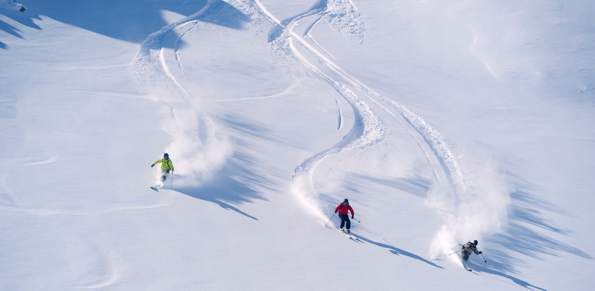 Three skiers offpisting with powder sprays behind them